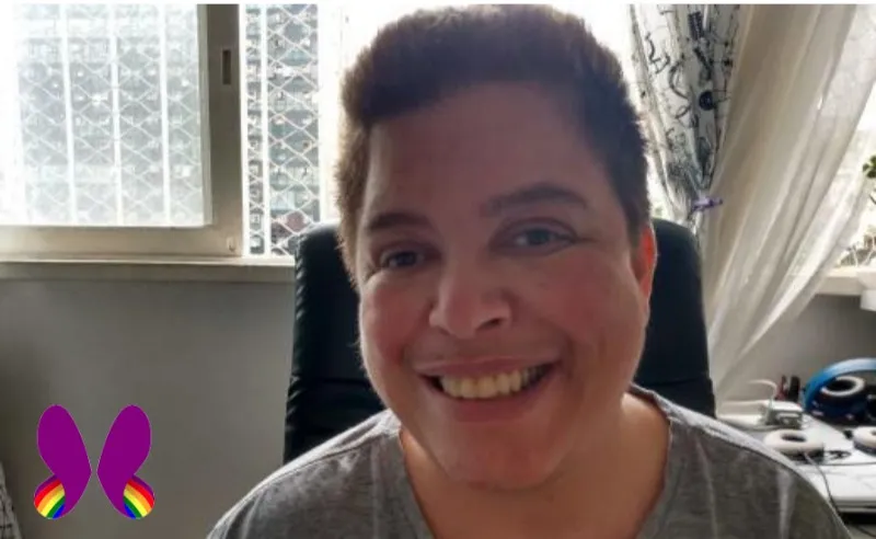 Foto de Amiel sentado e sorrindo. Ele é um homem branco de cabelos curtos e camisa cinza. Ao fundo, uma janela e cortinas.