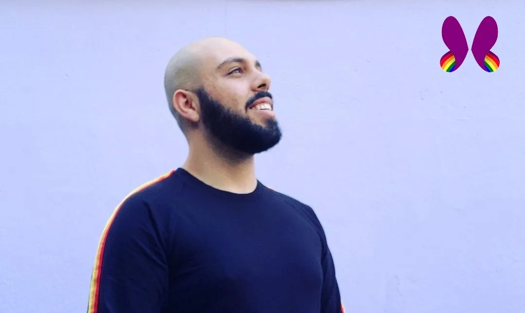 Foto de Cadu num fundo azul claro. Ele é um homem careca, tem barba, está sorrindo e usa uma camisa de mangas longas e detalhes coloridos nas laterais. No canto superior direito, a logo do projeto.